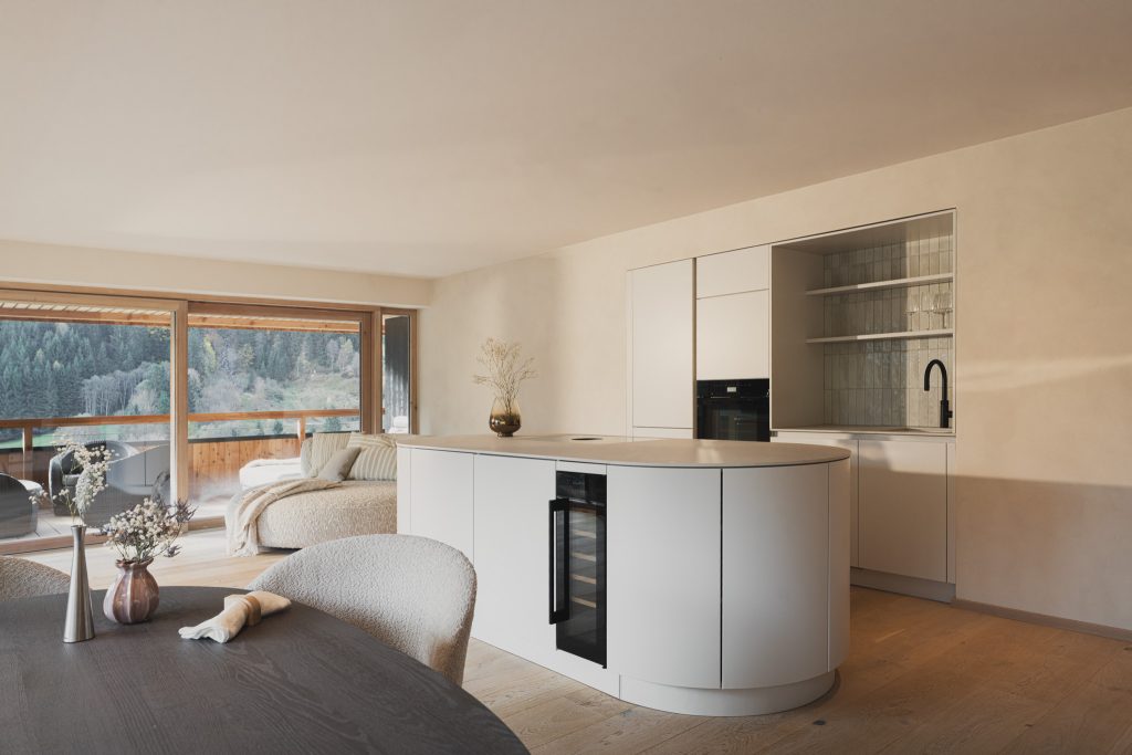 Appartementeinrichtung hell, Farbe Beige, Mittelpunkt ist die ovale Kochinsel, Ausschnitt von Essbereich - organische Form, Hintergrund Sofa Isla Stoff hell, Designappartement